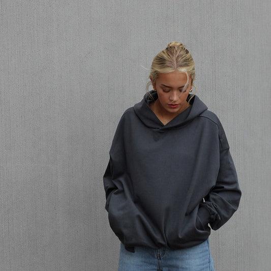 Woman standing against wall wearing dark grey hoodie
